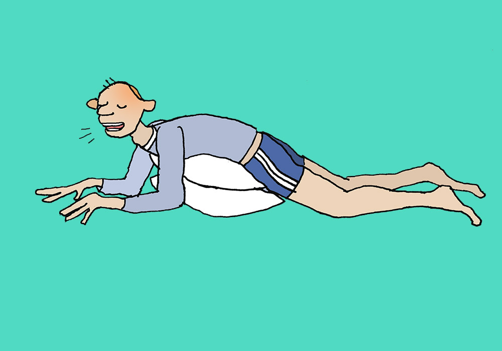 Mann liegt mit Bauch auf Kissen, atmet und übt Beckenschaukel